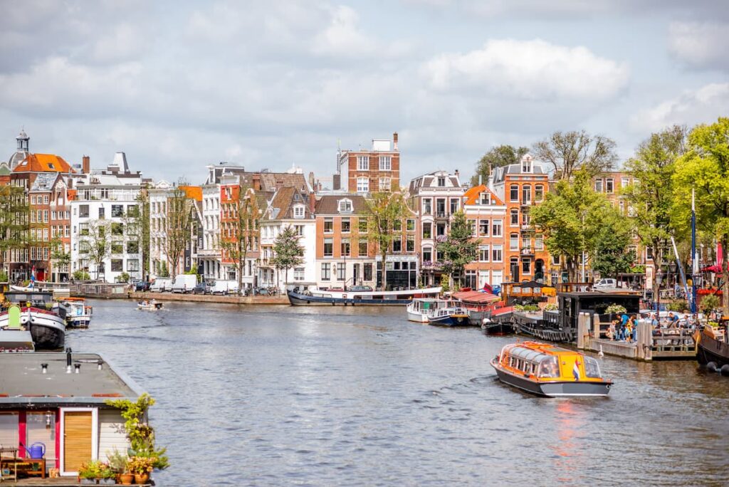 Imagem mostra lindas construções e barcos flutuantes pelos canais de Amsterdã. 