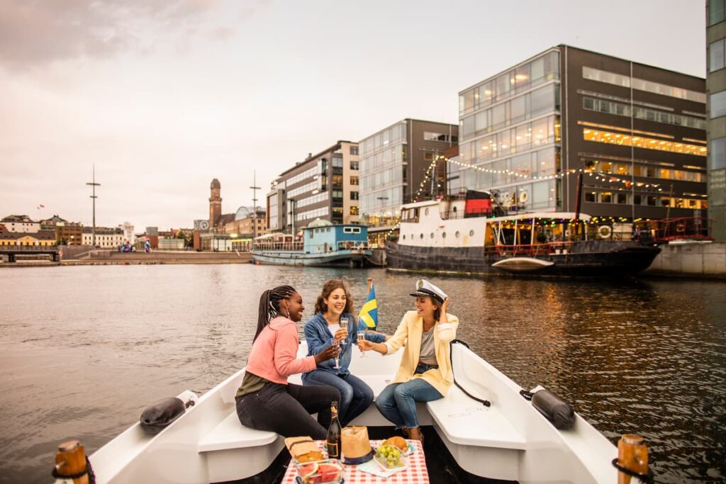 Imagem mostra jovens turistas em passeio de barco privativo pelos canais de Amsterdã.