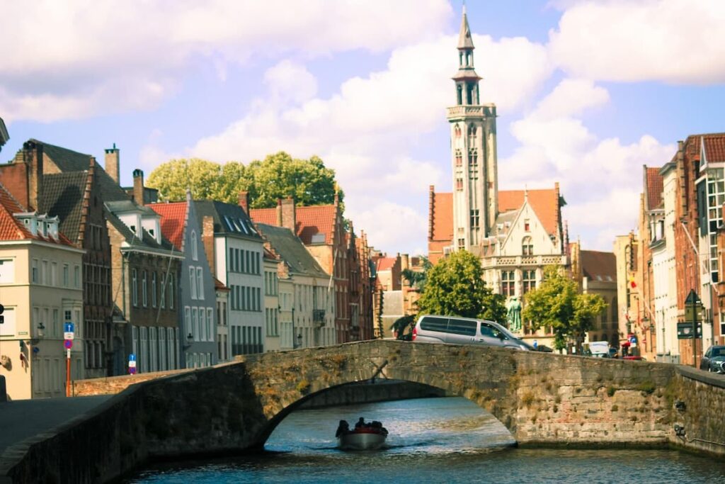 Imagem mostra ponte em Bruges e barco levando pessoas pelos canais da cidade mais linda da Bélgica.