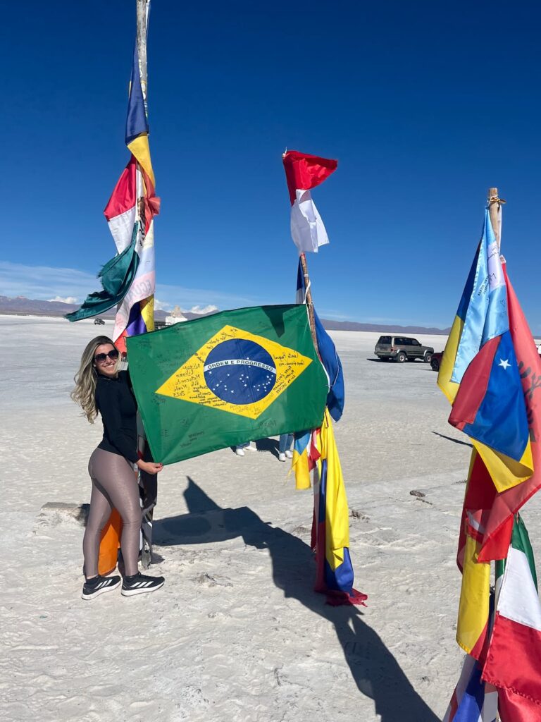 Imagem mostra turista fotografando com a bandeira do Brasil no Salar do Uyuni, Bolívia.