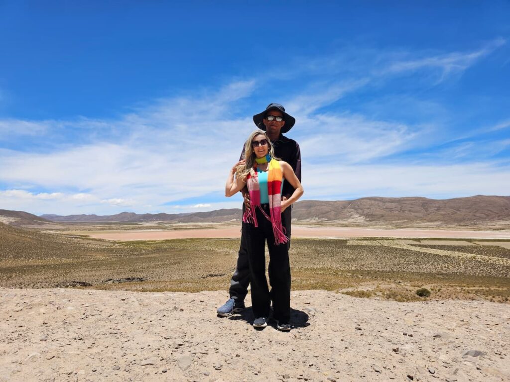 Imagem mostra casal passeando pelo altiplano boliviano. Ao fundo Laguna Colorada em época de seca.