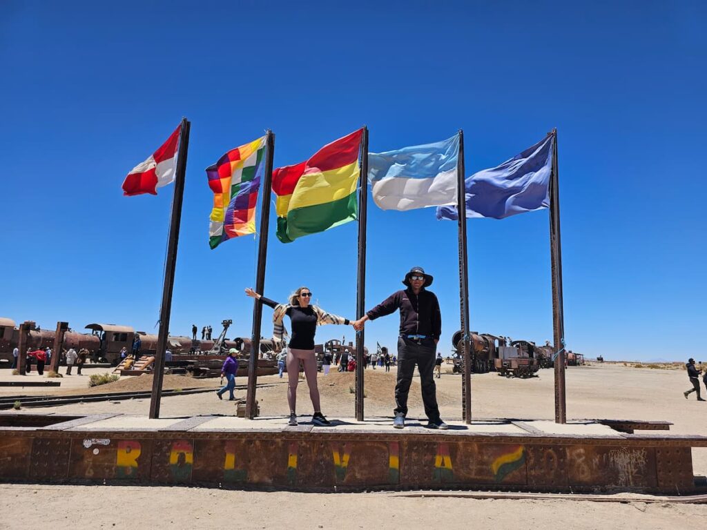 Imagem mostra casal no cemitério de trens, um dos passeios no Salar de Uyuni, Bolívia.